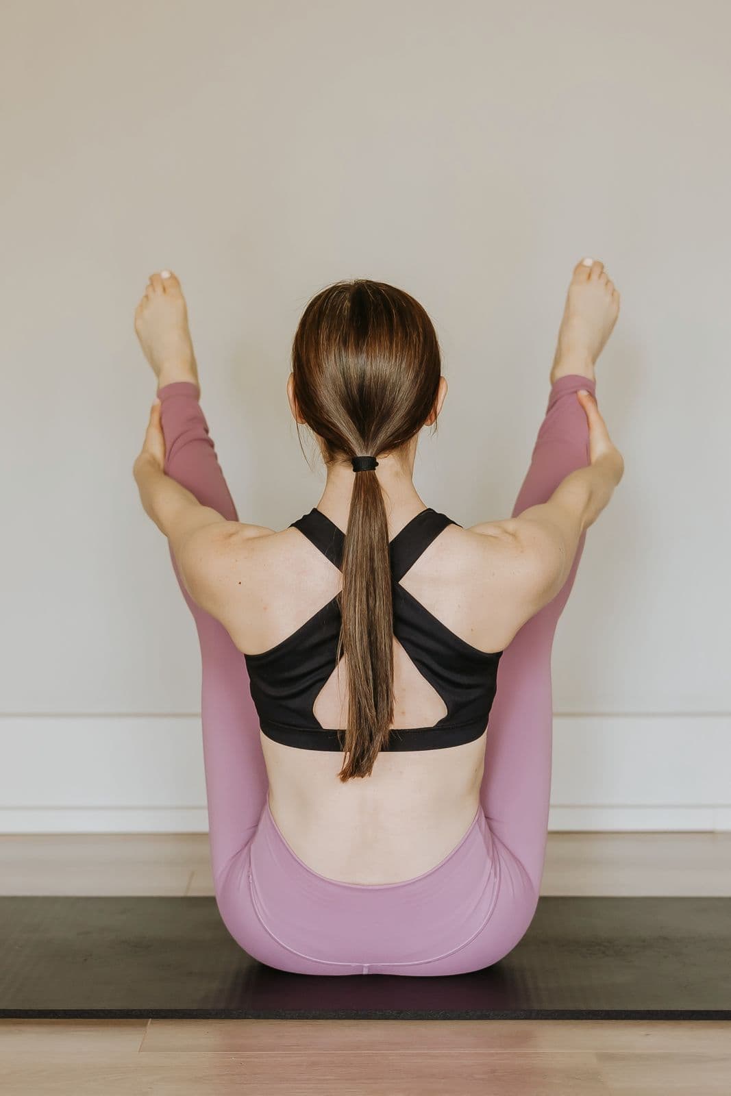 Siân balancing in open-leg rocker on a Pilates mat, seen from behind, legs lifted in a V